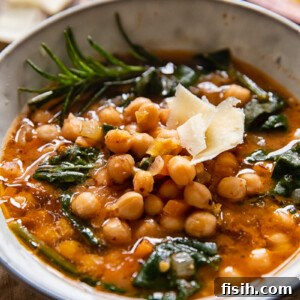 A rustic bowl of Tuscan Chickpea Soup garnished with fresh rosemary and grated hard cheese, highlighting its rich, savory texture.