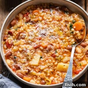 Overhead view of Sardinian Minestrone in a large pot with a spoon, showing an abundance of greens, grains, pasta, and beans in a vibrant tomato broth.