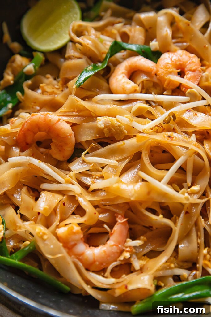 A close-up view of freshly cooked Shrimp Pad Thai, showcasing vibrant rice noodles, succulent shrimp, crisp bean sprouts, green onions, and a bright slice of lime.