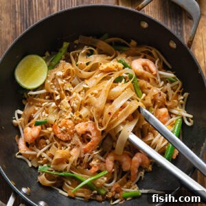 wok with pad Thai, with tongs removing a portion, next to a lime and peanuts