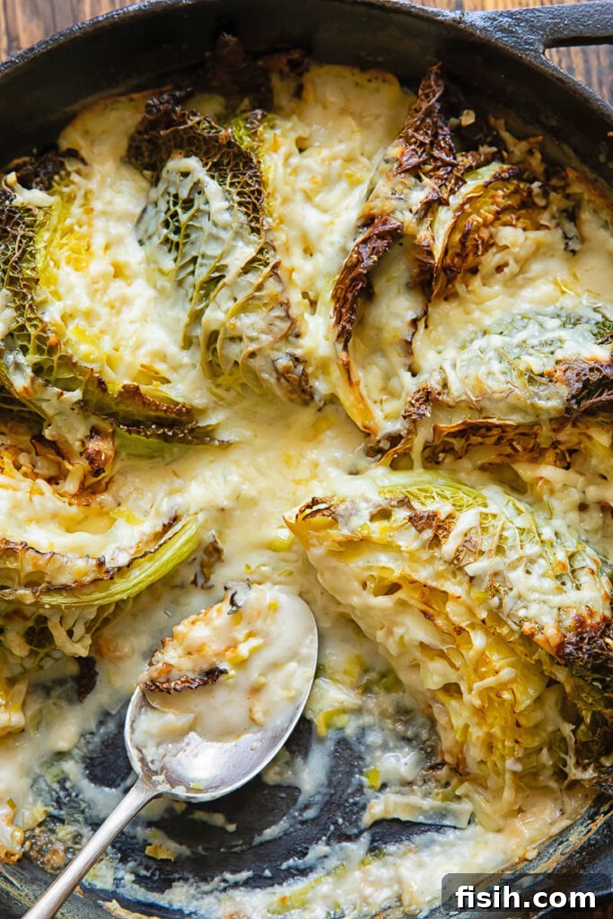 Close up of a skillet with wedges of savoy cabbage in a creamy sauce, garnished with herbs.