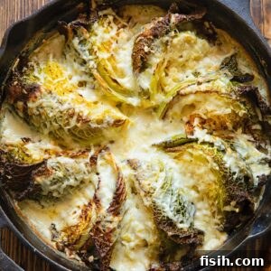 Cast iron skillet with cabbage wedges arranged in a fan and covered by a creamy sauce, close up.