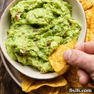 bowl of guacamole with hand dipping tortilla chip in