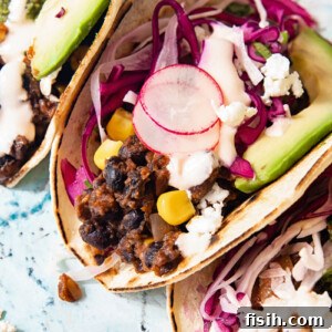 Close up of a black bean and corn taco showing radish and cilantro lime slaw and slice of avocado