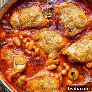 Top-down view of a rich Italian rosemary chicken stew served in a rustic pan, garnished with fresh herbs.