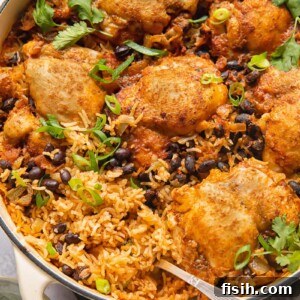 Top-down shot of Mexican chicken and rice in a pan, generously topped with black beans and fresh cilantro.