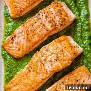 11 Vibrant Salmon Recipes Perfect for Sunny Days 3 A pan-seared salmon fillet topped with a vibrant green basil pesto sauce, served on a white plate.