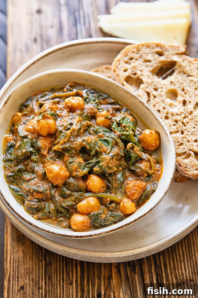 A rustic bowl of Spanish spinach and chickpea stew, served with slices of crusty bread on a plate.