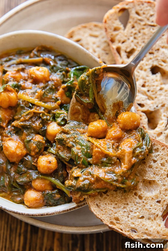 A spoon scooping a portion of spinach and chickpea stew from a bowl onto a piece of bread.