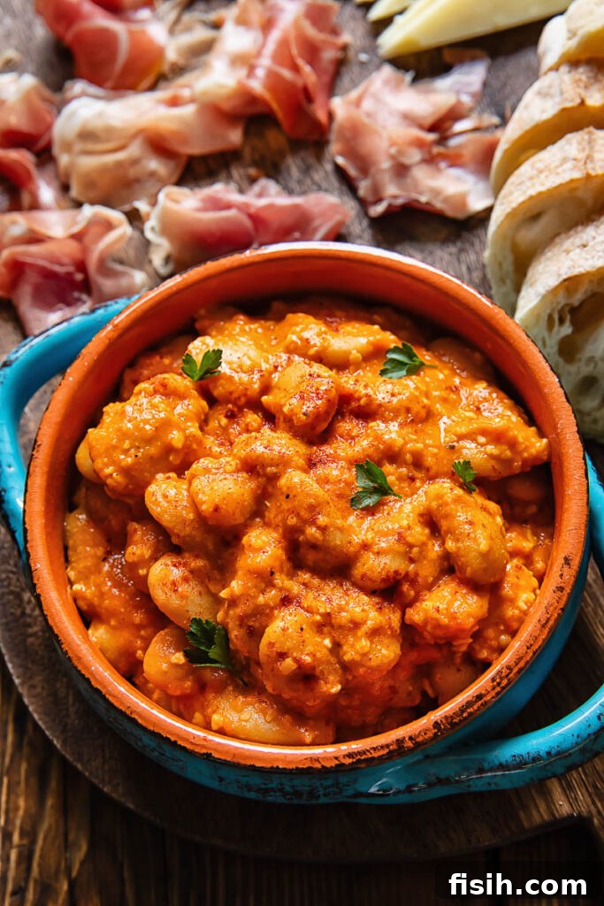 A close-up view of Spanish butter beans in a rich, red Romesco sauce, served in a traditional earthenware dish.