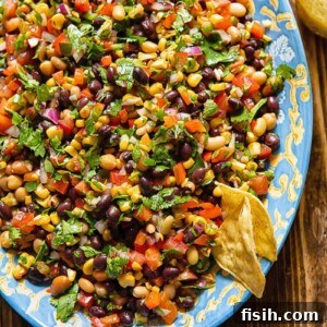 Top down shot of cowboy caviar on a large serving dish with beans, corn, pepper and tomatoes topped with dressing and fresh herbs
