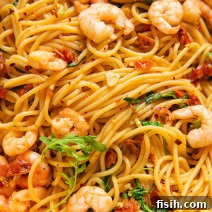 Close up shot of shrimp and spaghetti with sun dried tomato and chilli sauce topped with arugula