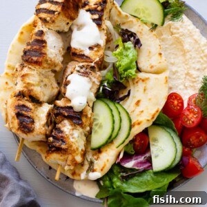 chicken souvlaki skewers on top of pita bread filled with hummus and vegetables