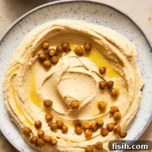 top down view of hummus spread on a light blue plate, topped with chickpeas and olive oil