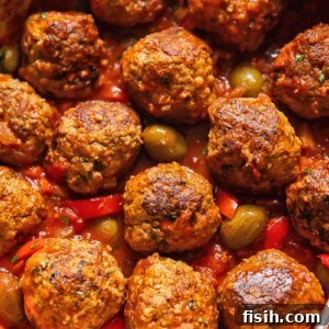 Top down shot of pork and beef meatballs in a pot with tomato sauce topped with olives and red pepper slices