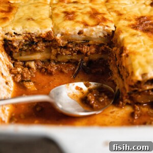 Close up shot of moussaka layers of beef and eggplant topped with creamy bechamel sauce along with a spoon