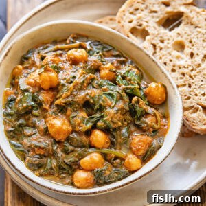 Top down view of a bowl of chickpeas and spinach, on top of a serving plate with a couple slices of bread.