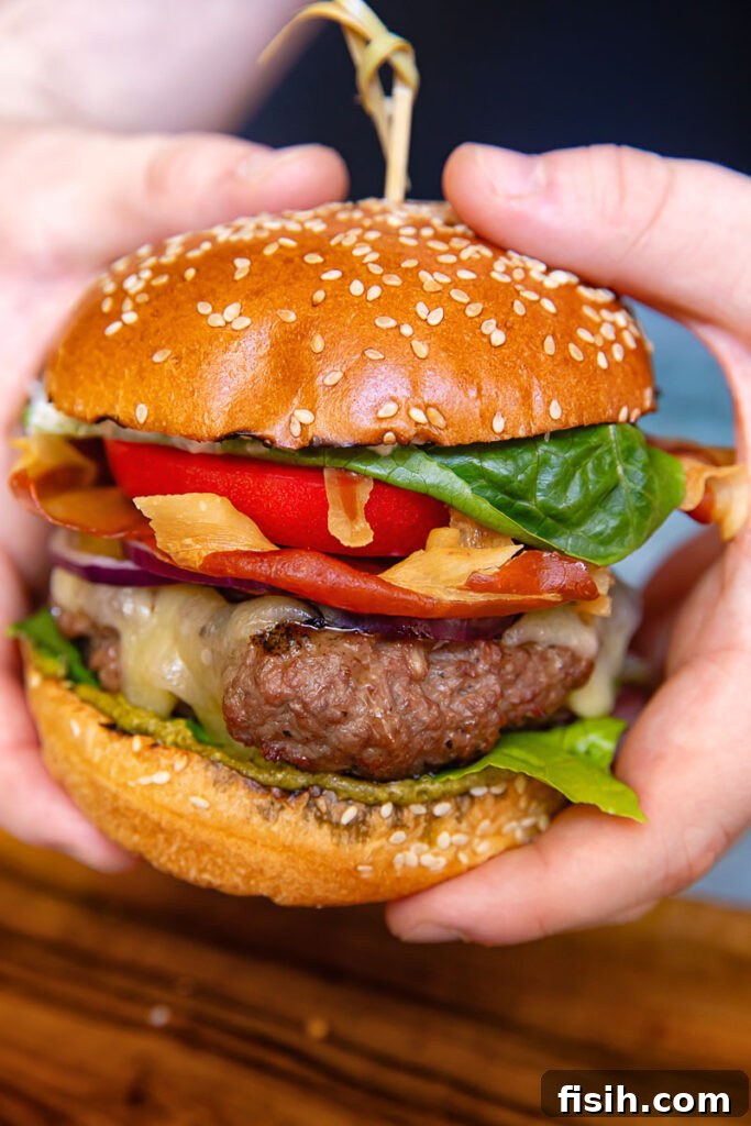 Italian Prosciutto Burger with Garlic Parmesan Mayo 2 A vertical shot of a beef patty, tomato, lettuce and prosciutto in a bun in hands