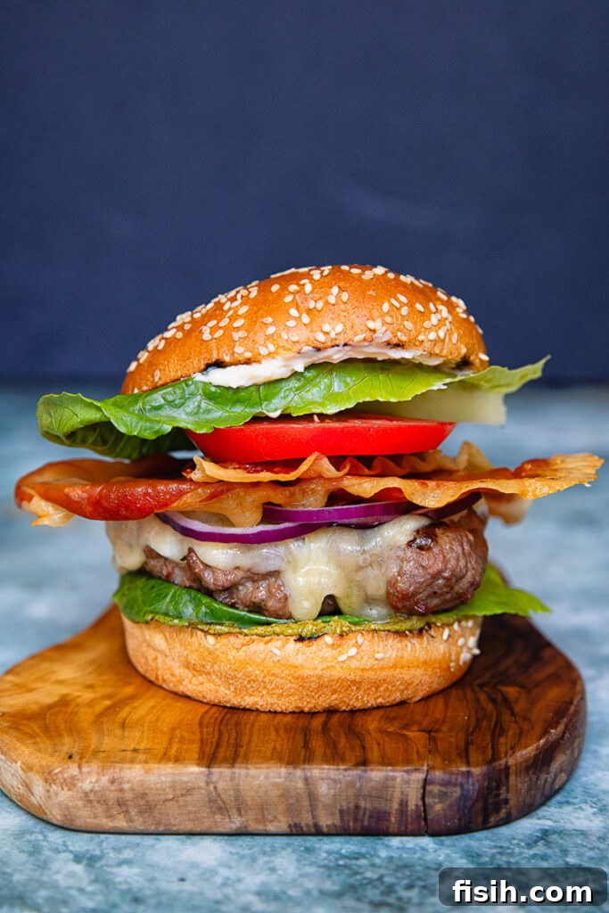 Italian Prosciutto Burger with Garlic Parmesan Mayo 4 A vertical shot of a beef patty, tomato, lettuce and prosciutto in a bun against a dark background