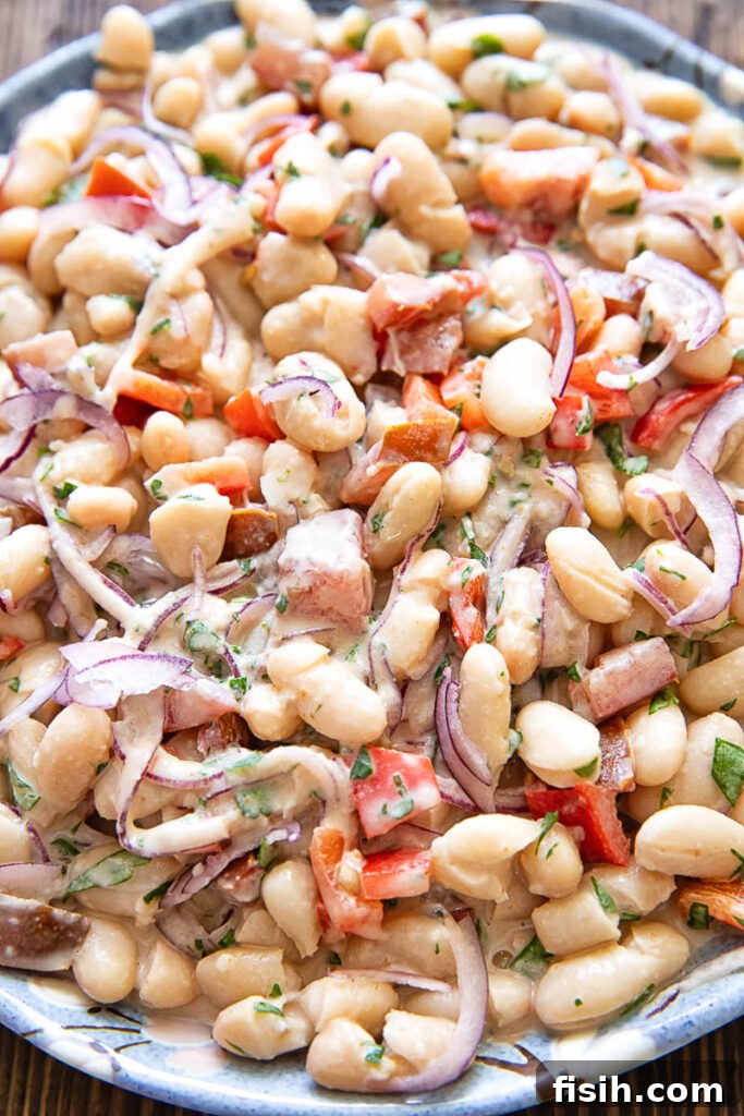 close up photo of the salad showing beans, onions and peppers with herbs and a creamy dressing.