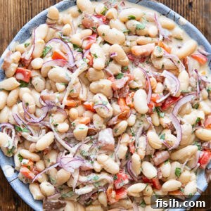 Top down photo of the bean salad in a white bowl on a dark wood background.