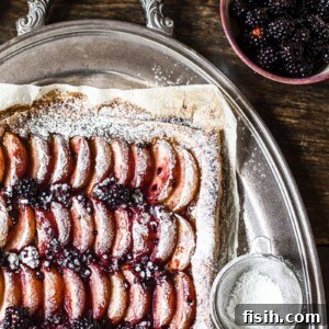 Corner of the tart next to icing sugar and blackberries