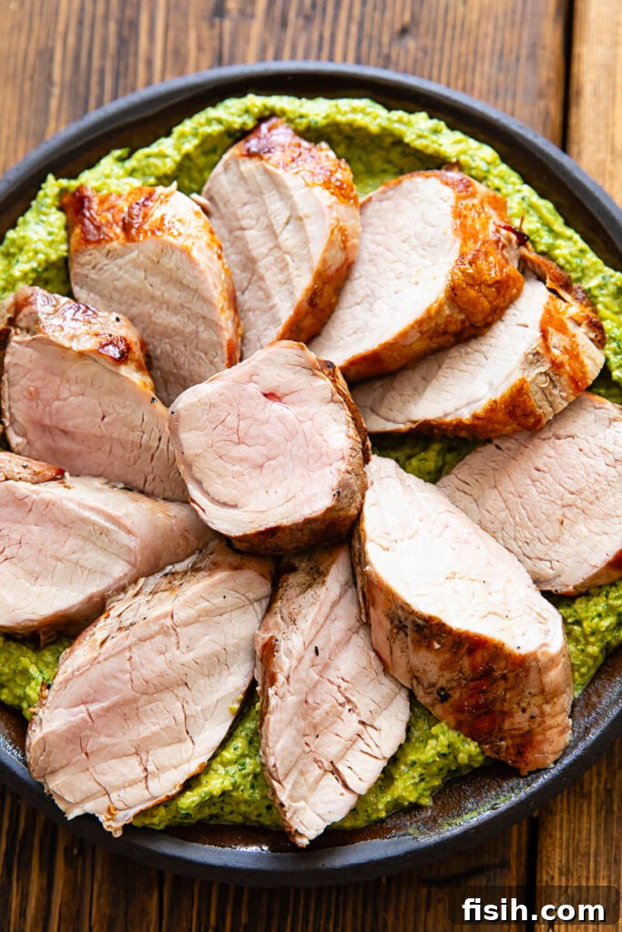 Grilled Pork Tenderloin with Green Romesco 3 Slices of pork tenderloin on a bed of green sauce, on a plate with a dark wood background.