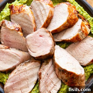 Grilled Pork Tenderloin with Green Romesco 5 Slices of pork tenderloin on a bed of green sauce, on a plate with a dark wood background.