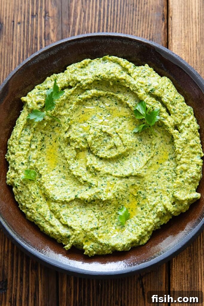 Green Romesco Sauce Recipe for Grilled Vegetables and Fish 2 Green romesco sauce with herbs spread on a dark plate with a wooden background.