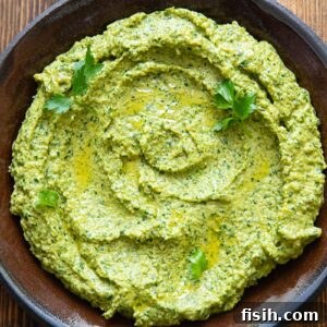 Green romesco sauce with herbs spread on a dark plate with a wooden background.