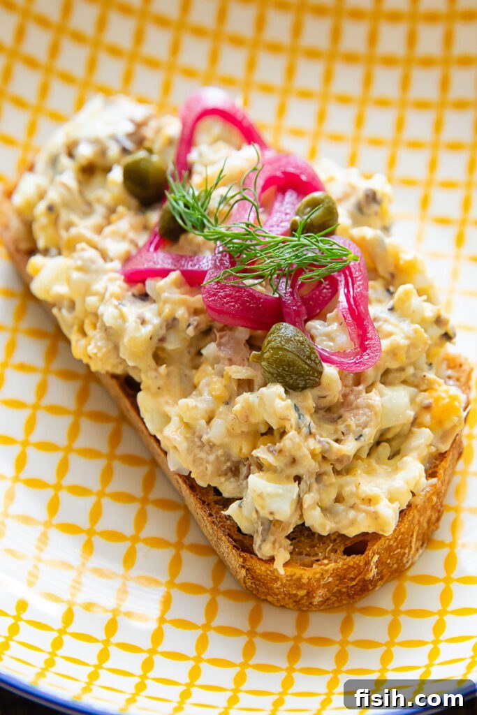 3 Sardine Toast Recipes: Flavorful Ideas for Any Meal 4 Toast on a yellow striped plate topped by a sardine mixture, capers, pickled onion and dill.
